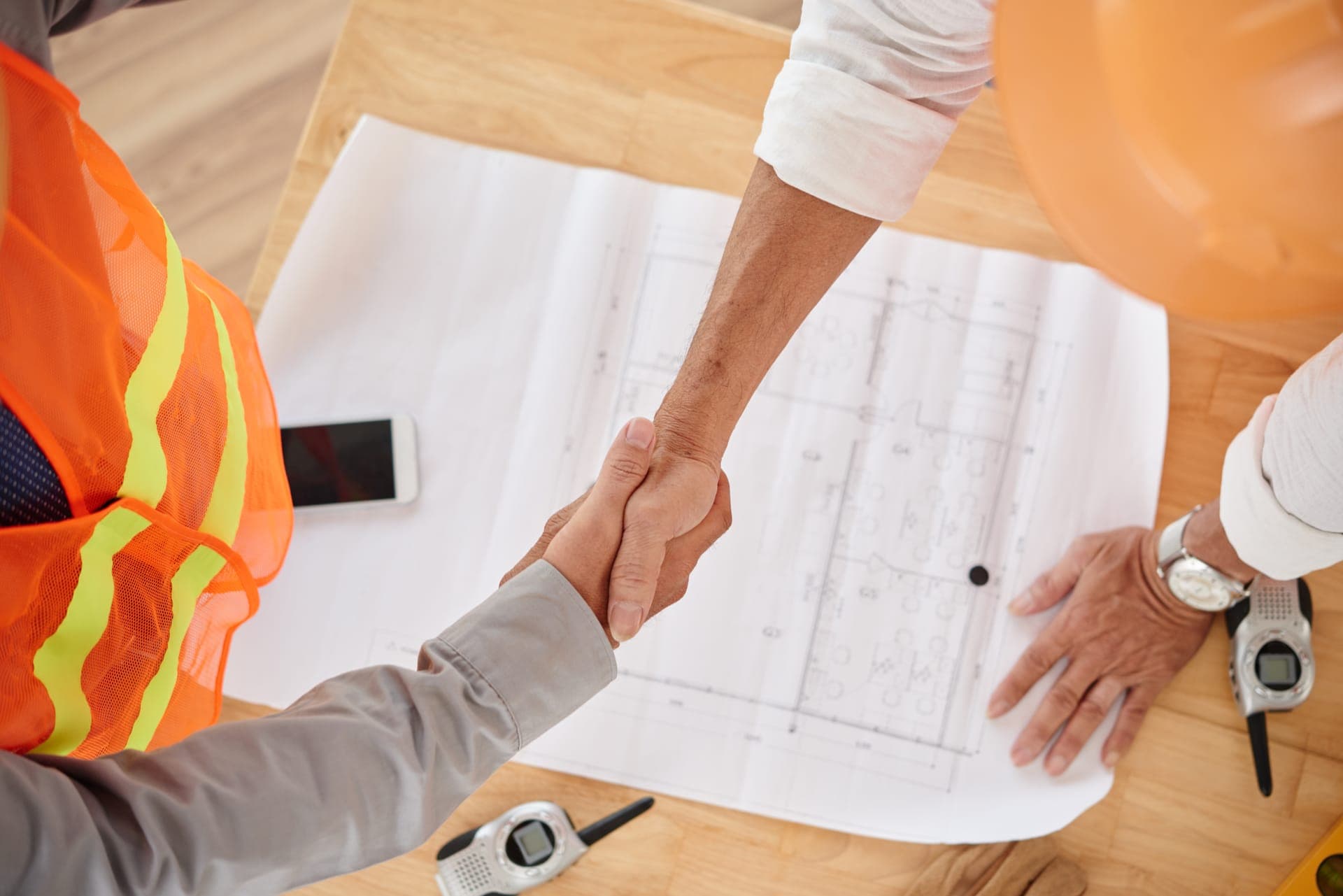 Handshake over blueprints between ARRT Roofing and a homeowner