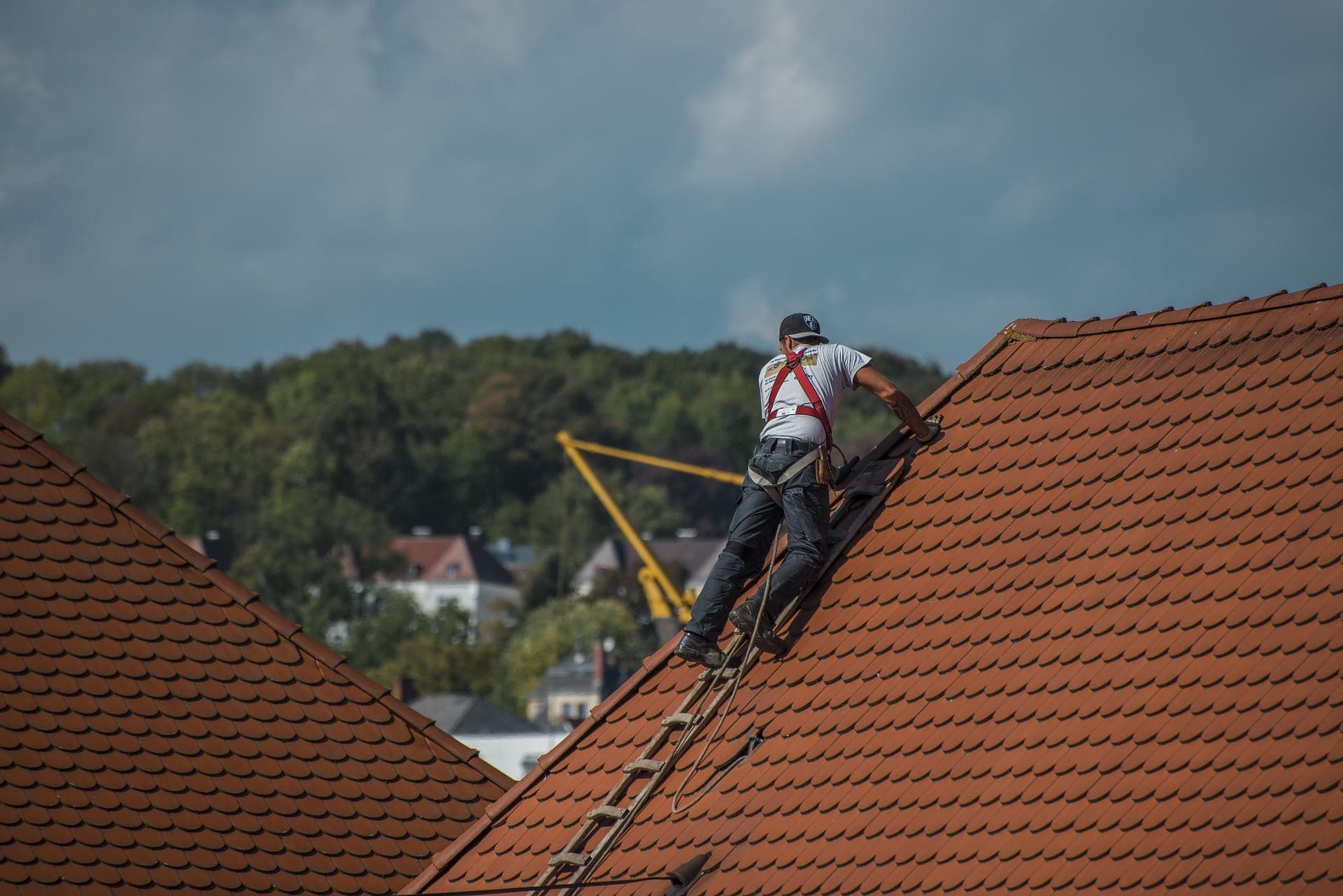 Roofer in safety harness working on a steep tiled roof
