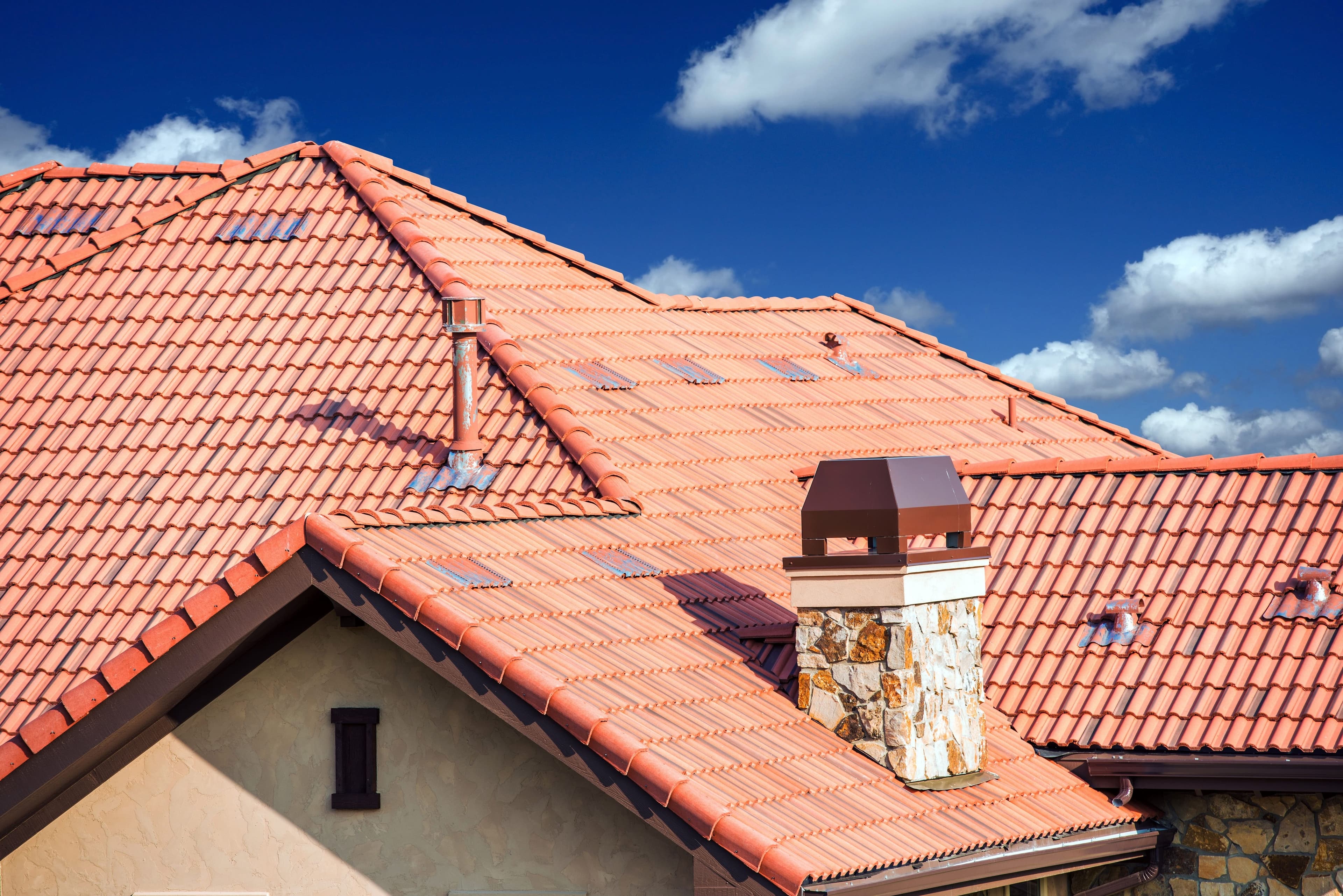 Terracotta tile roof with stone chimney against a blue sky
